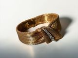 a close up of a gold bracelet with a bow on it