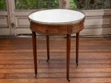 une petite table ronde avec un plateau en marbre posée sur un parquet