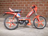 a small red motorcycle parked in front of a brick wall