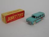 une petite voiture Dinky Toy avec une boîte de jouets Dinky Toys posée sur une surface blanche