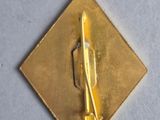 a gold pin with a knife on it on a white surface