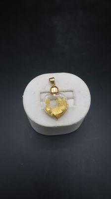 a gold heart pendant on a white marble surface
