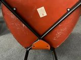 an orange chair with two crossed legs and a tag on it