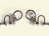 two pairs of silver earrings with pearls hanging from them on a white surface