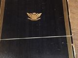 an old black book with a gold emblem on it sitting on a wooden table