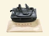black leather handbag sitting on top of a bag on top of a white bag