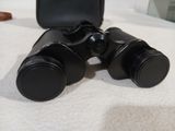 une paire de jumelles posée sur un lit, à côté d'un étui