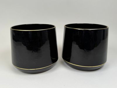 deux tasses noires aux bords dorés posées sur un fond blanc