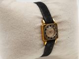 an image of a gold and black watch sitting on a pillow