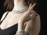 a woman in a black dress with pearls on her arm