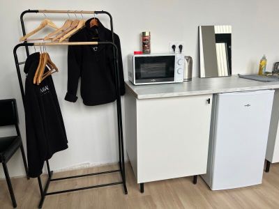 a small kitchen with a microwave, refrigerator, and clothes rack