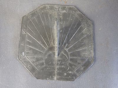 un cadran solaire en métal posé sur un tissu blanc, sur une table