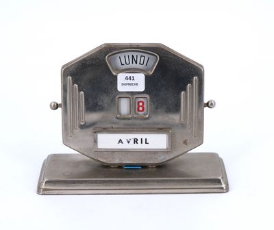 une horloge en argent posée sur un socle, sur une surface blanche