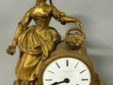a gold clock with a woman sitting on top of it