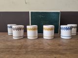 four white cups with blue and yellow designs are lined up on a wooden table