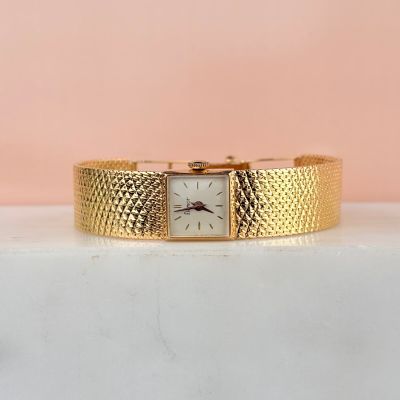gros plan d'une montre-bracelet en or sur une surface blanche