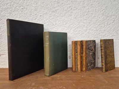 several old books are lined up on a table next to a white wall