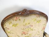 une chaise en bois avec un dossier et des accoudoirs rembourrés d'un motif floral