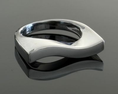 bague en argent posée sur une surface réfléchissante, avec un reflet sur cette surface