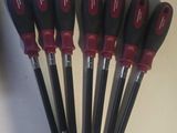 six outils noirs et rouges sont alignés sur une surface blanche