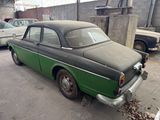 an old green car parked in a parking lot next to other cars