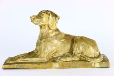 statue dorée représentant un chien, posée sur un socle en bois, sur fond blanc