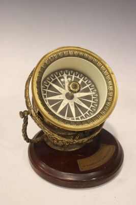 une boussole ancienne en laiton posée sur un socle en bois, sur fond blanc
