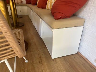 a white bench with red pillows on it in the corner of a room