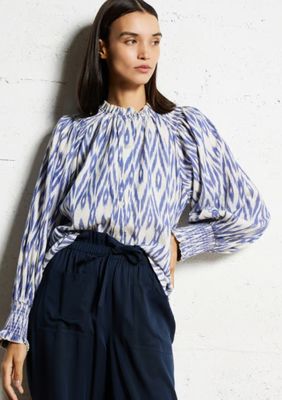 an image of a woman standing against a wall wearing a blue and white blouse