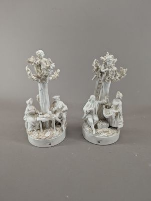 une paire de figurines en porcelaine blanche représentant un homme et une femme assis sous un arbre