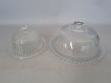 two clear glass dishes with lids on a white surface