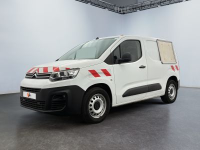 La camionnette blanche est garée dans une grande pièce ; elle porte une bande rouge sur le côté.
