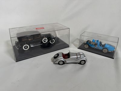 trois petites voitures dans une vitrine posée sur une surface blanche