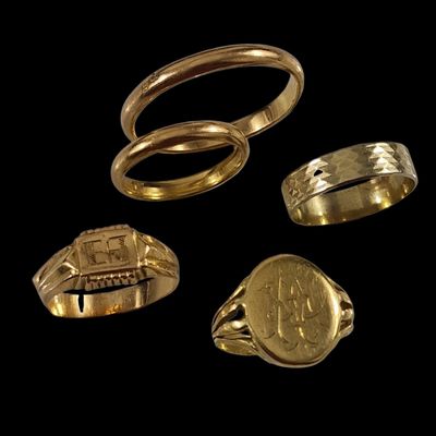 trois bagues en or et une bague ornée d'une pièce de monnaie sur fond noir