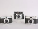 three old cameras sitting side by side on a white surface