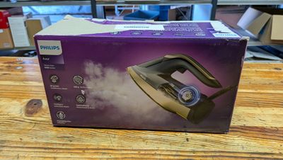 une boîte ouverte contenant un fer à repasser à vapeur, posée sur une table en bois