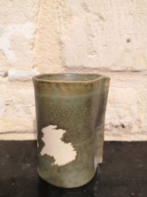 une tasse verte posée sur une table noire, avec un mur de briques en arrière-plan
