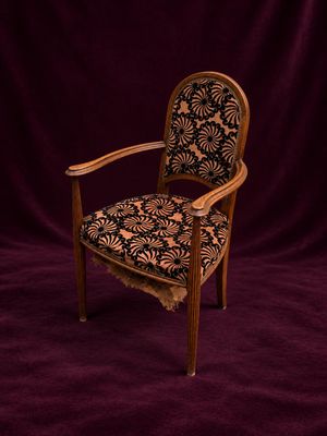 une vieille chaise dont l'assise est recouverte d'un tissu à motifs floraux sur fond violet