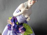 a figurine of a woman wearing a purple dress and holding flowers