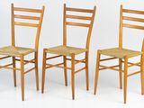 three wooden chairs sitting next to each other on a white surface