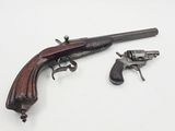 an old gun and a small revolver on a white surface