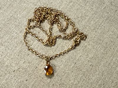a close up of a necklace with a gold chain and a glass bead