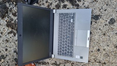 an open laptop computer sitting on the ground next to a cell phone