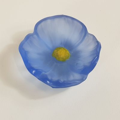 une fleur en verre bleue au cœur jaune, posée sur une surface blanche