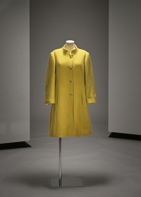 un manteau jaune posé sur un porte-manteau dans une pièce aux murs blancs