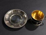 silver cup and saucer on a black table with a black background