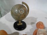 un petit globe terrestre posé sur un socle, à côté d'une poupée et d'un ours en peluche