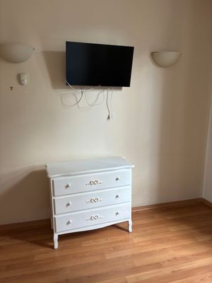 une commode blanche dans une pièce où est accrochée une télévision à écran plat au mur