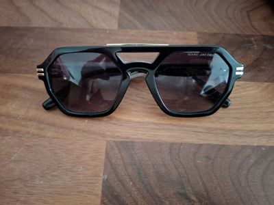 des lunettes de soleil noires posées sur un parquet, sur fond marron