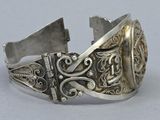 silver bracelet with a design on the side of it on a white surface